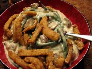 A red bowl filled with creamy green bean casserole topped with crispy fried onion strips and pieces of chicken, with a silver spoon resting on the side.