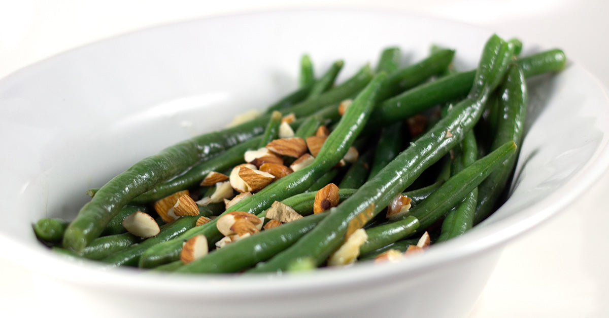 Bowl of cooked green beans topped with chopped almonds.