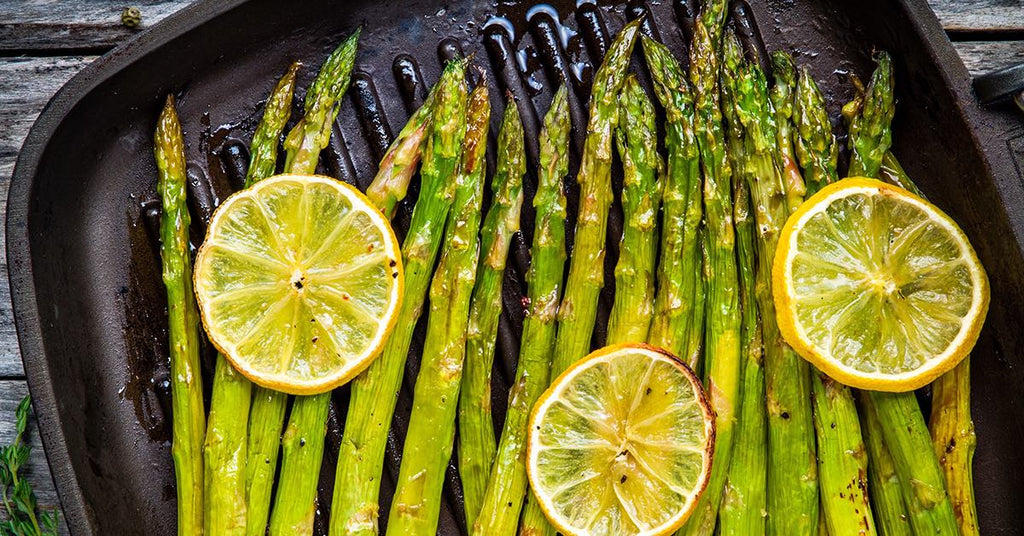 Grilled asparagus spears topped with lemon slices in a grill pan.