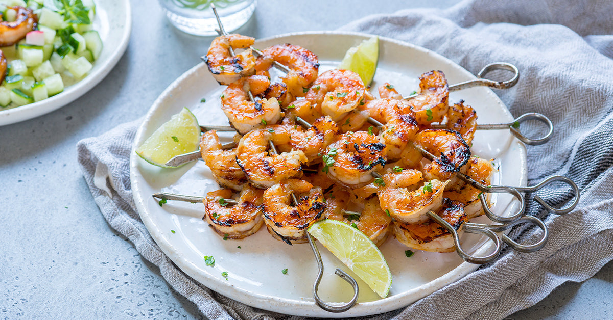 Grilled shrimp skewers served on a plate with lime wedges and fresh herbs.