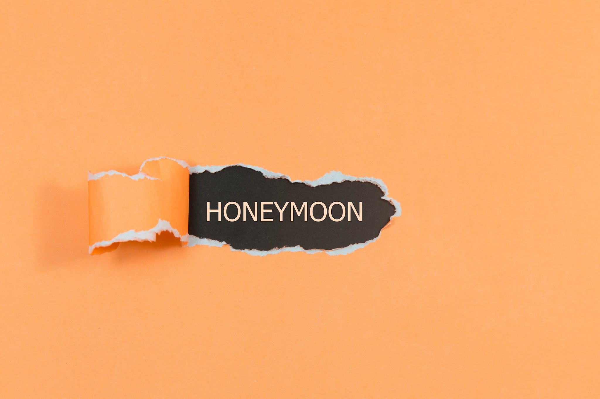 Torn orange paper revealing the word HONEYMOON on a black background.