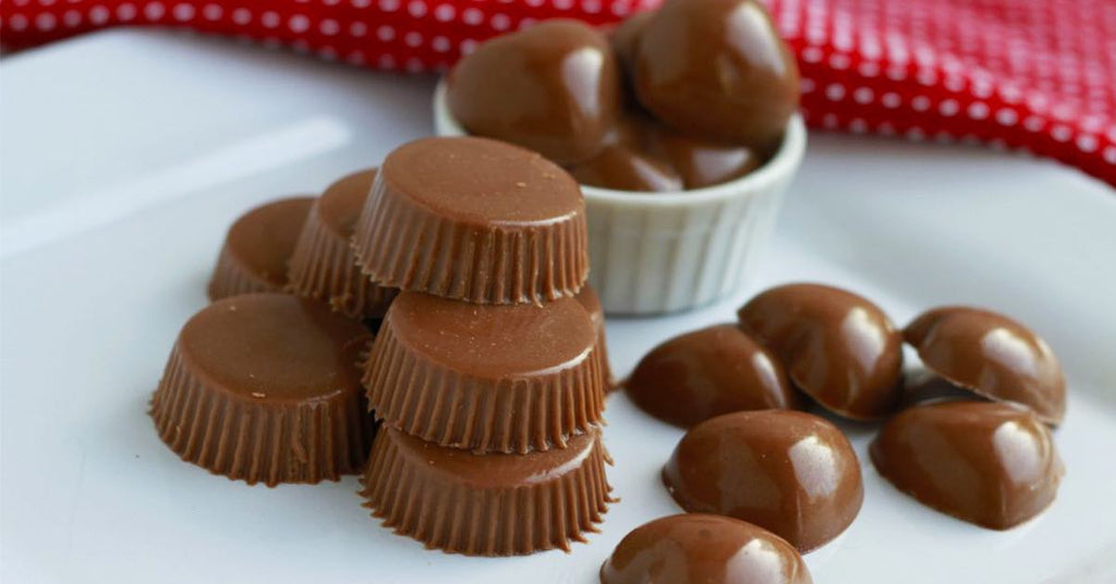 Stacks of smooth, glossy chocolate cups and domes arranged on a white plate.