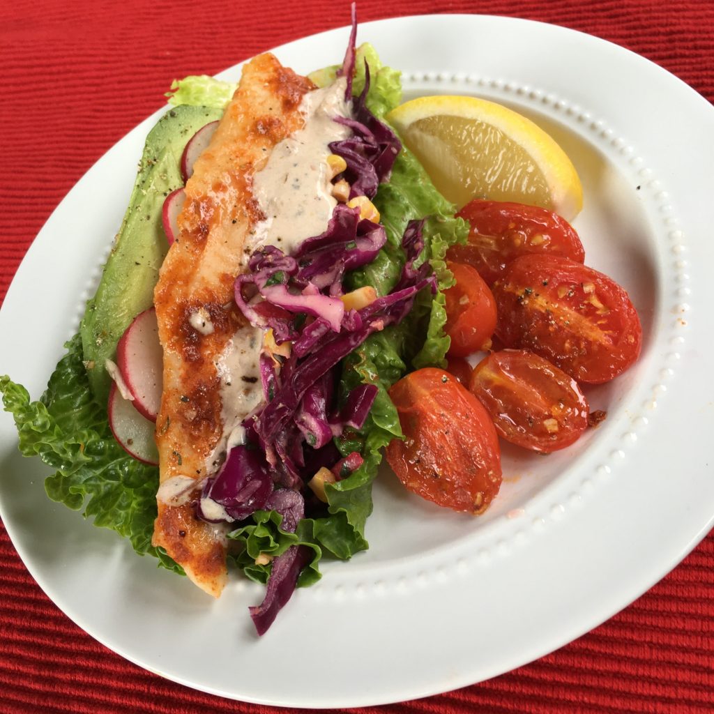 Grilled chicken lettuce wrap with avocado, radish, and purple slaw, served with roasted cherry tomatoes and lemon.