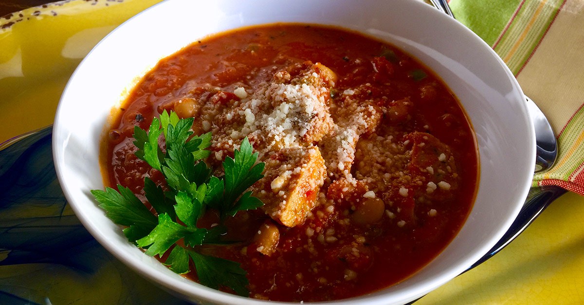 Hearty tomato-based soup topped with grated cheese and fresh parsley in a white bowl.