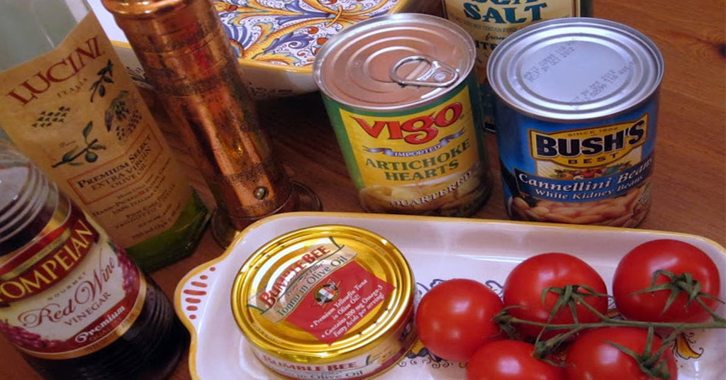 Assorted pantry items including canned beans, artichoke hearts, tuna, olive oil, vinegar, spices, and fresh tomatoes.