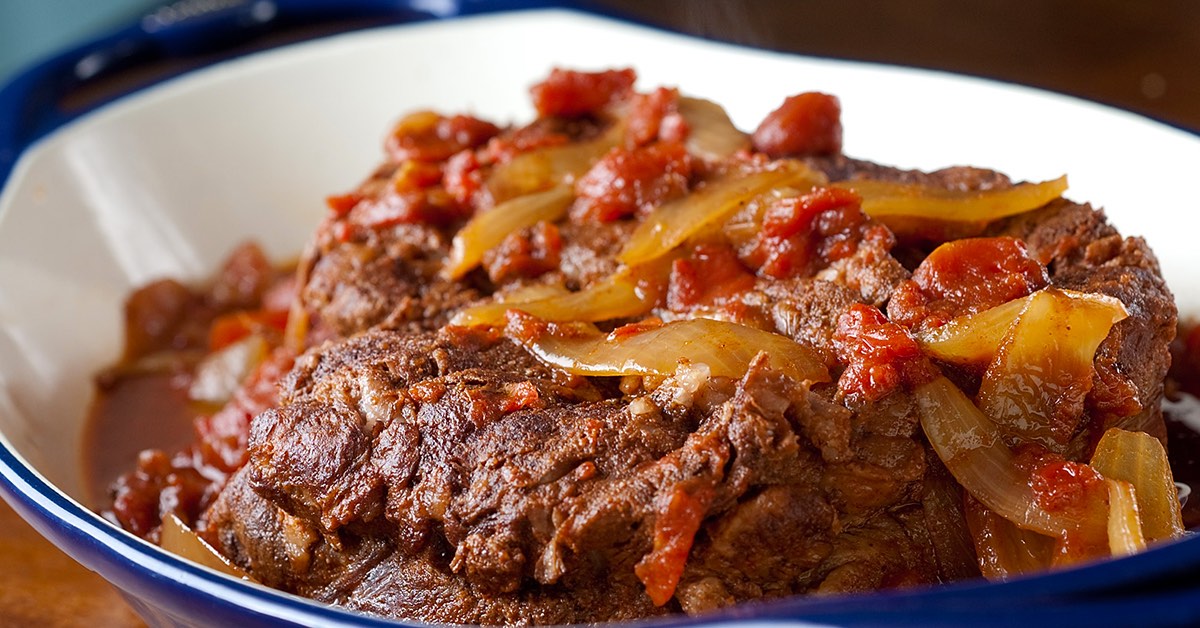 Slow-cooked beef roast topped with sautéed onions and diced tomatoes in a rich, savory sauce.