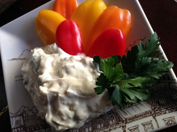 Creamy dip served on a plate with colorful mini peppers and a sprig of fresh parsley.