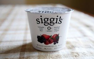 A container of Siggi's yogurt labeled "Mixed Berries & Acai" sits on a checkered tablecloth, showcasing its creamy texture and vibrant fruit illustrations on the front.