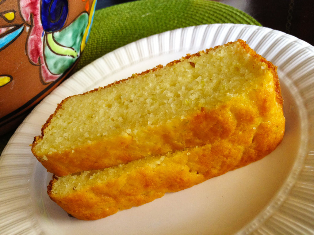 Two slices of moist, golden-yellow cake with a soft crumb, served on a white plate beside a colorful ceramic pot.