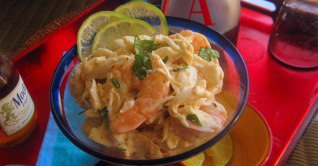Creamy shrimp salad with cilantro and lime slices served in a glass bowl on a red tray.