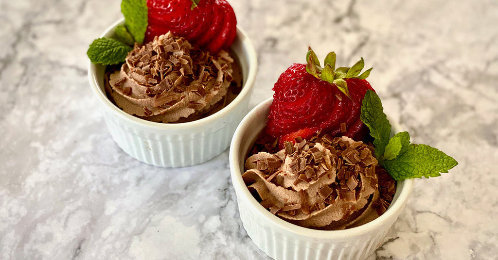 Two cups of chocolate mousse topped with chocolate shavings, fresh strawberries, and mint leaves.