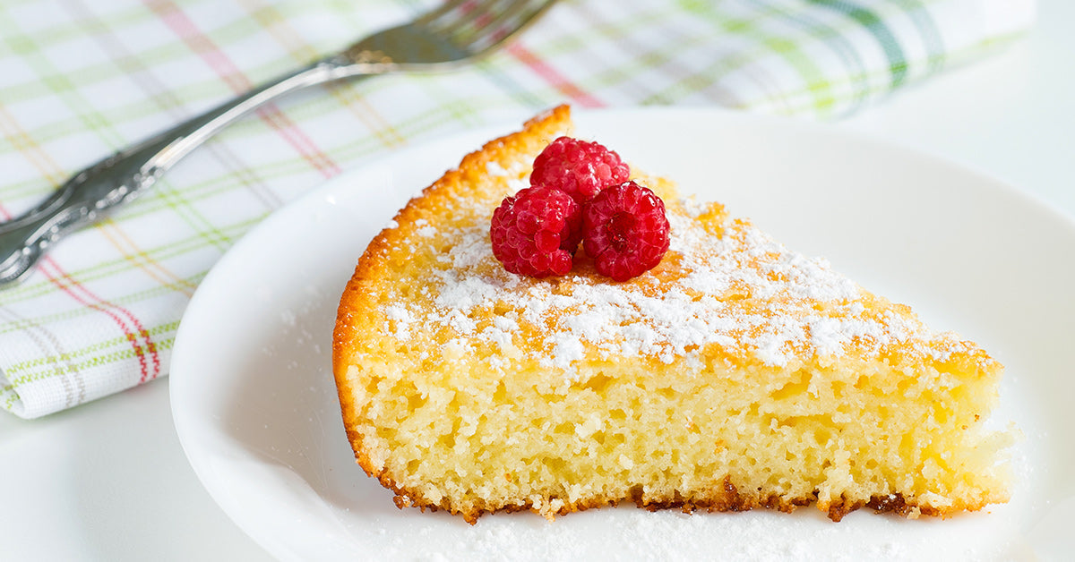 Slice of powdered sugar topped cake garnished with fresh raspberries on a white plate.