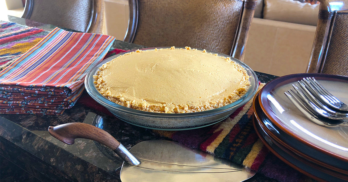 A creamy pie in a glass dish on a table with colorful napkins, plates, forks, and a pie server.