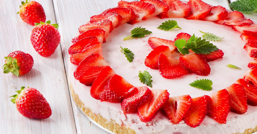 Strawberry cheesecake topped with fresh sliced strawberries and mint leaves on a white wooden surface.