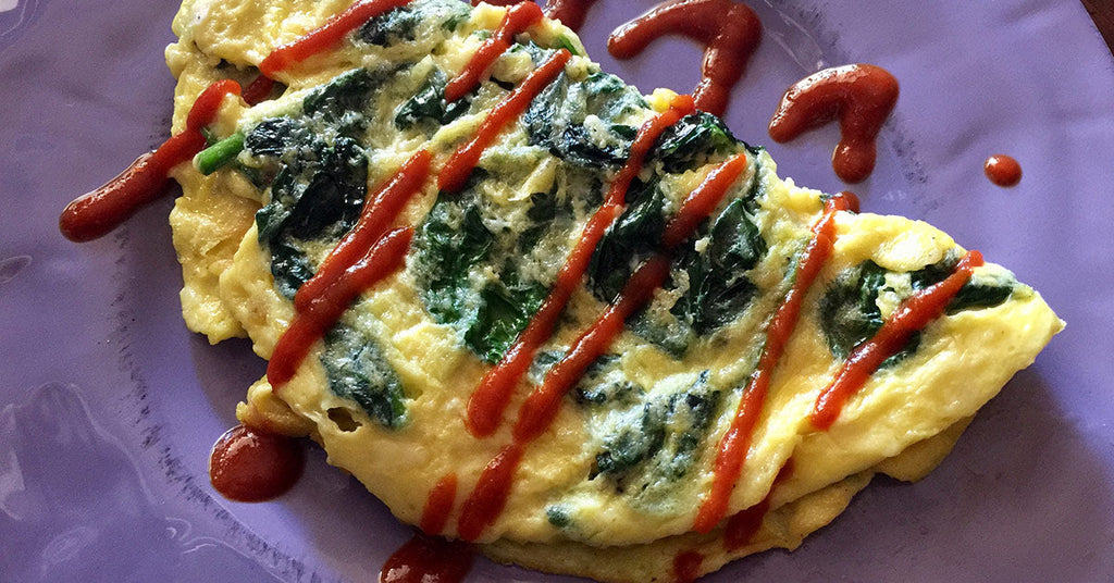 Spinach omelet on a purple plate topped with zigzagged red sauce.
