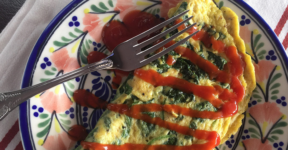 Spinach omelet on a floral plate topped with zigzag ketchup and a fork resting on top.