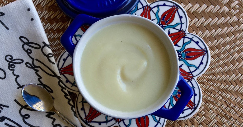 Creamy white soup served in a blue-handled bowl on a patterned plate with a spoon and napkin nearby.