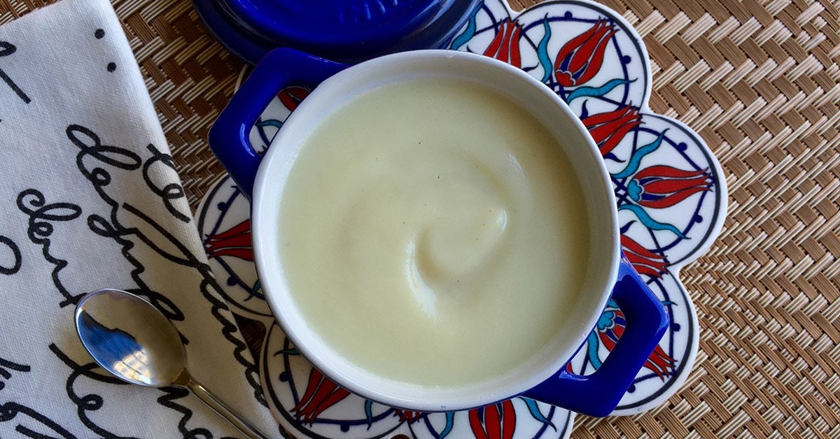 Creamy white soup served in a blue-handled bowl on a patterned plate with a spoon and napkin beside it.