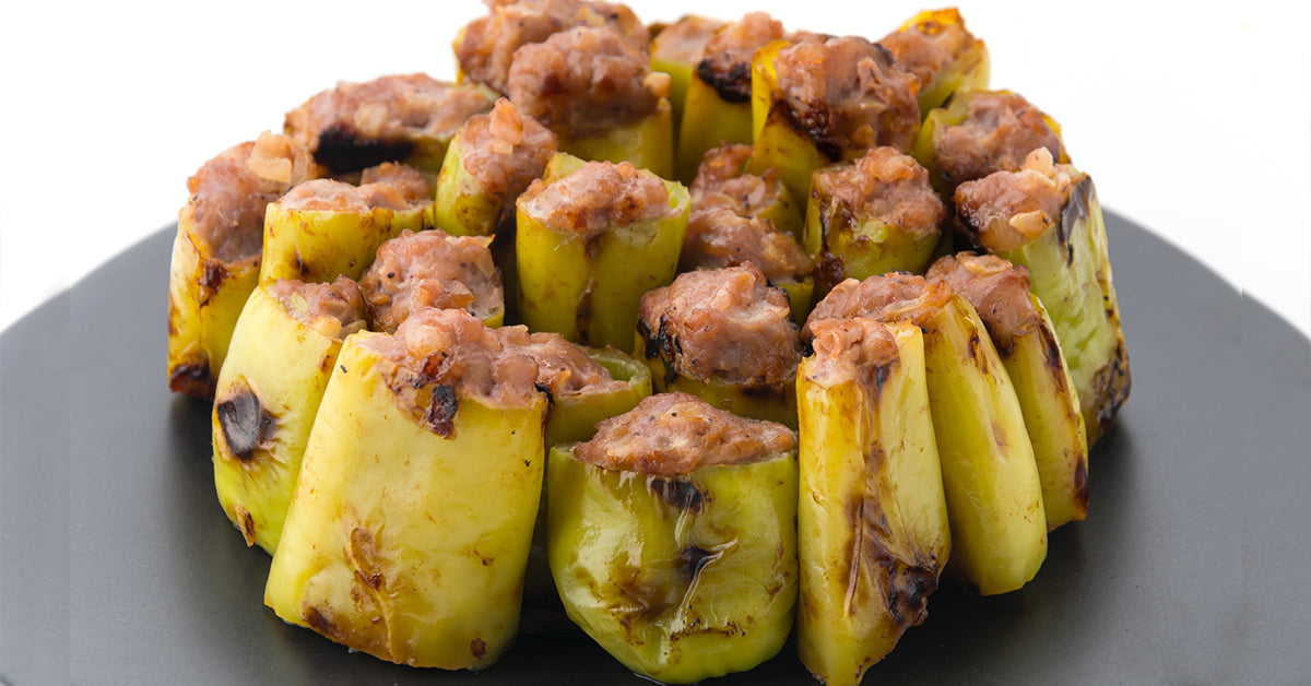 Stuffed green chili pieces filled with minced meat, arranged upright in a circular pattern on a black plate.
