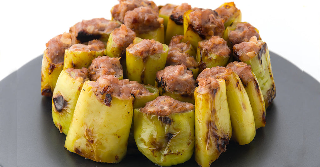 Stuffed green chili pieces filled with minced meat, arranged upright in a circular pattern on a black plate.