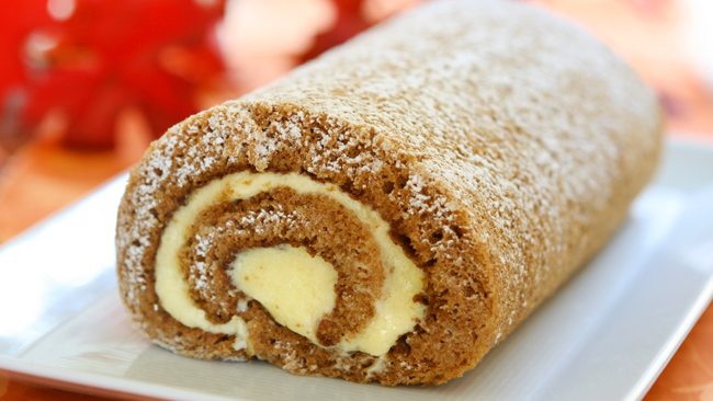 Soft pumpkin roll cake dusted with powdered sugar and filled with creamy spiced frosting.
