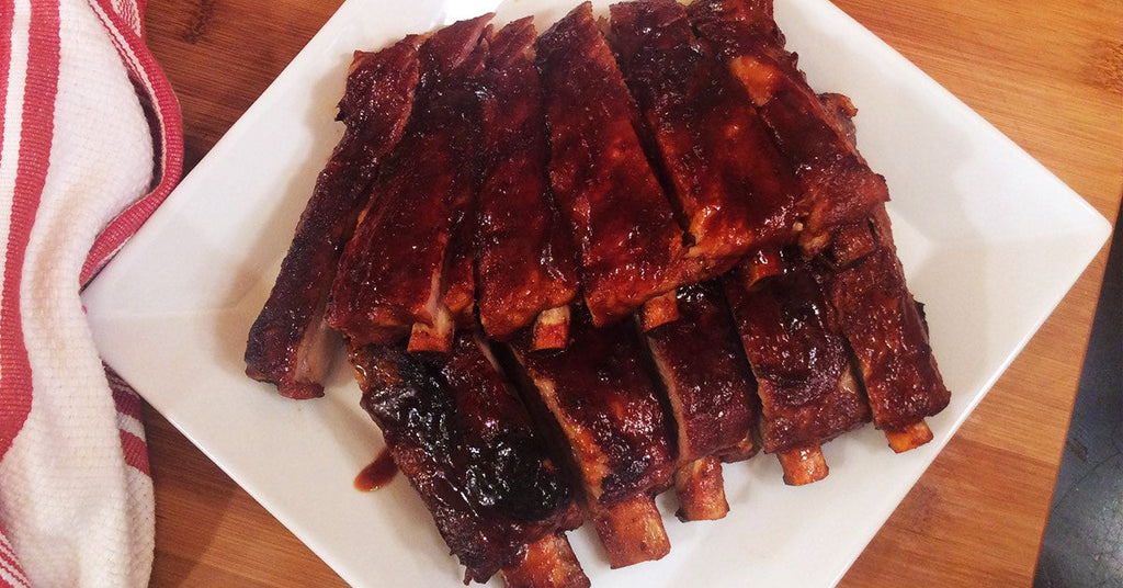 Plate of glazed, barbecued ribs arranged in rows on a white square dish.