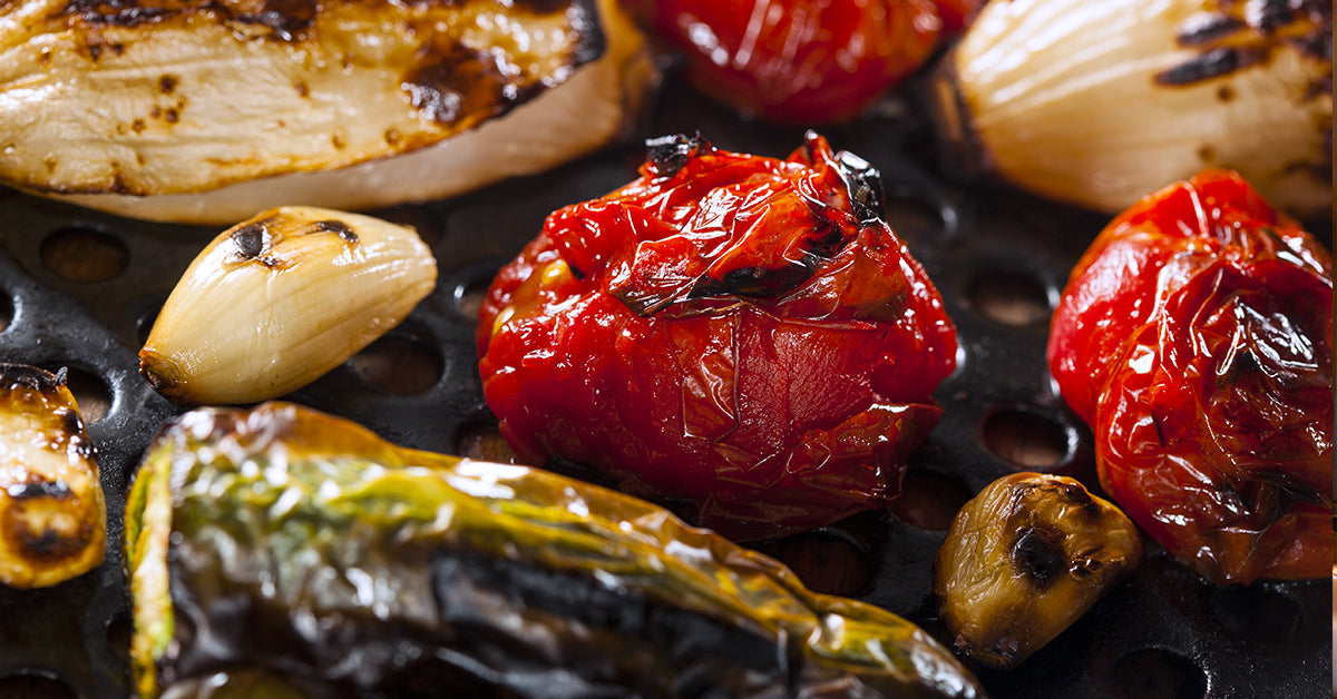 Charred tomatoes, garlic, and peppers roasting on a grill plate.