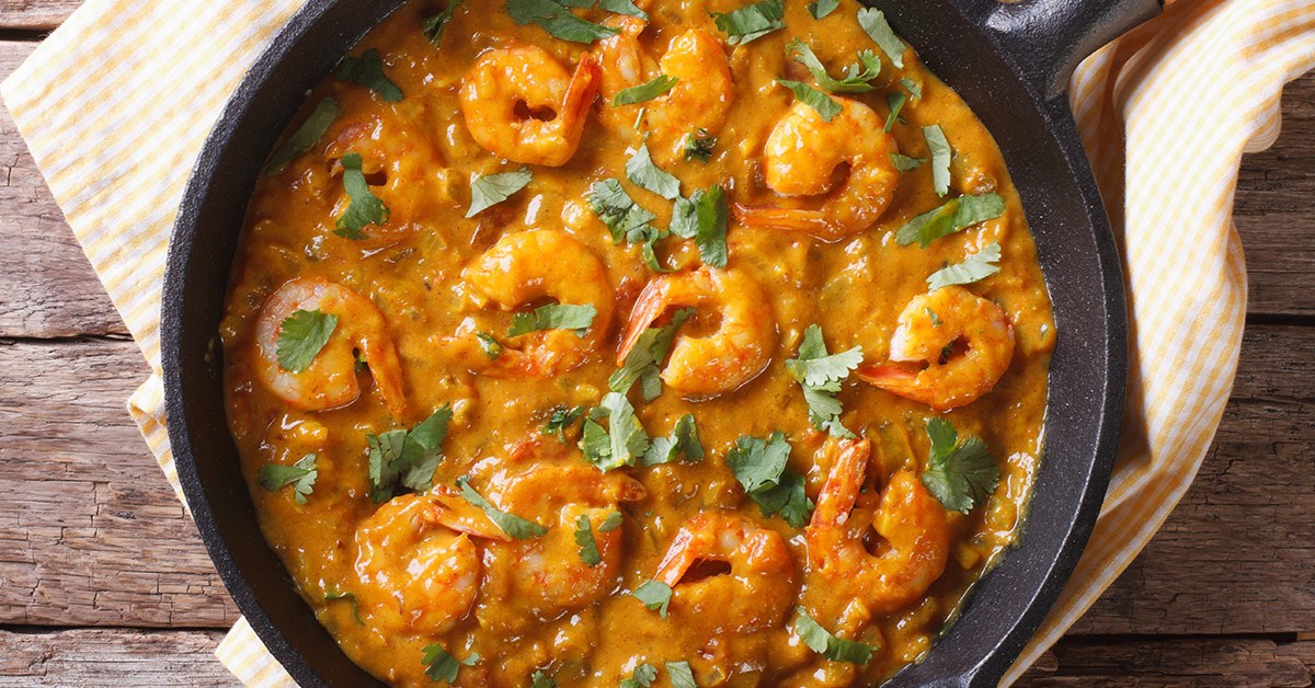 Shrimp cooked in a creamy orange curry sauce, garnished with fresh cilantro in a black skillet.