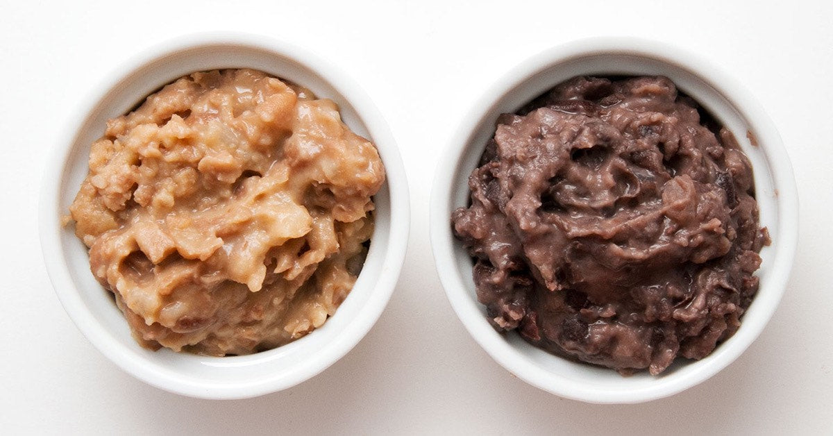 Two small white bowls filled with creamy refried beans, one light and one dark in color, on a white background.