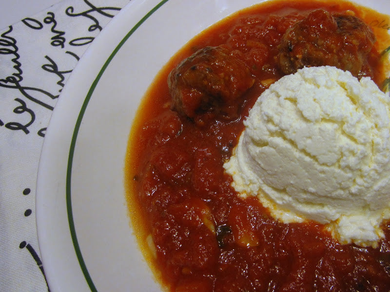 Bowl of tomato sauce with meatballs and a large scoop of ricotta cheese on the side.