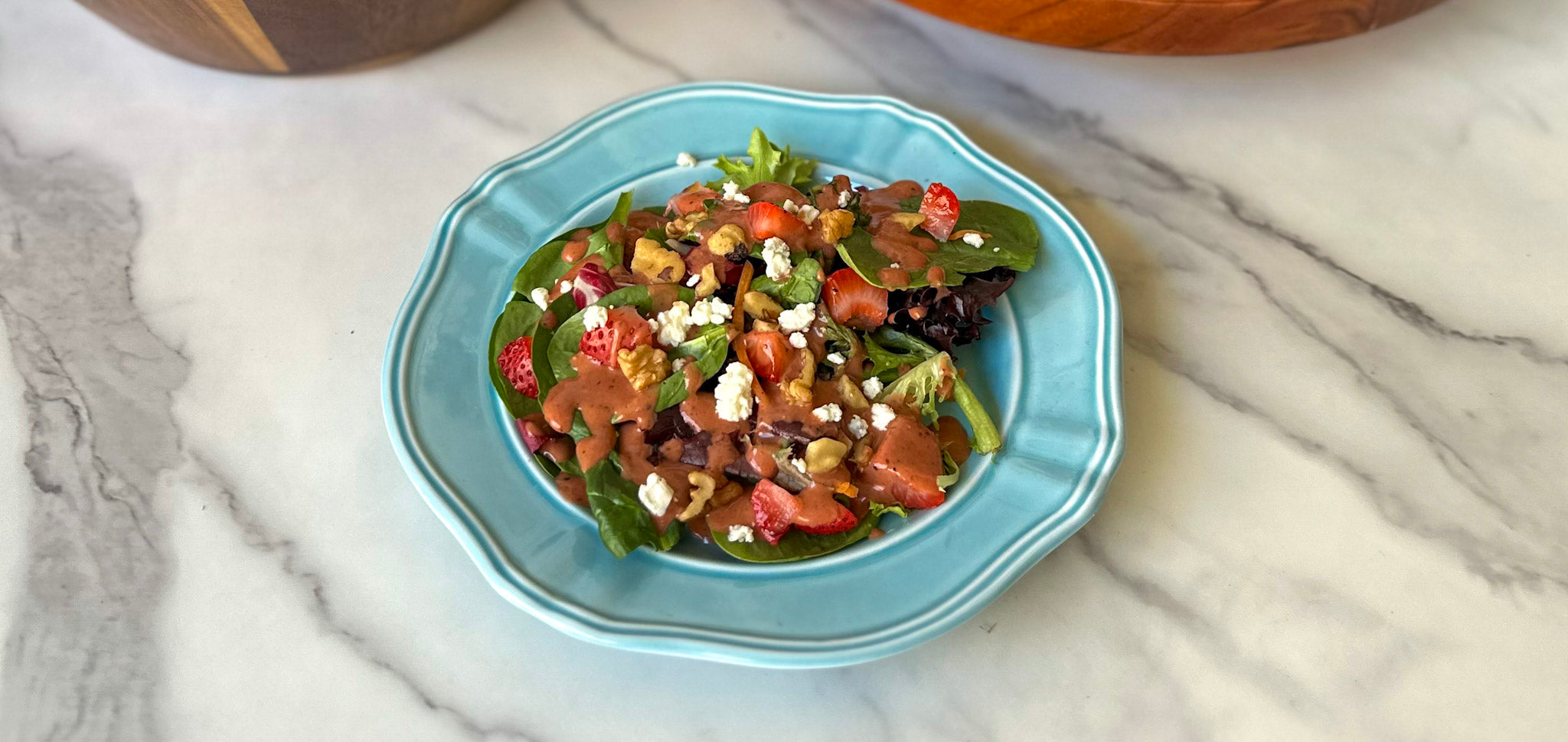 Strawberry spinach salad with feta, nuts, and dressing served on a light blue plate.