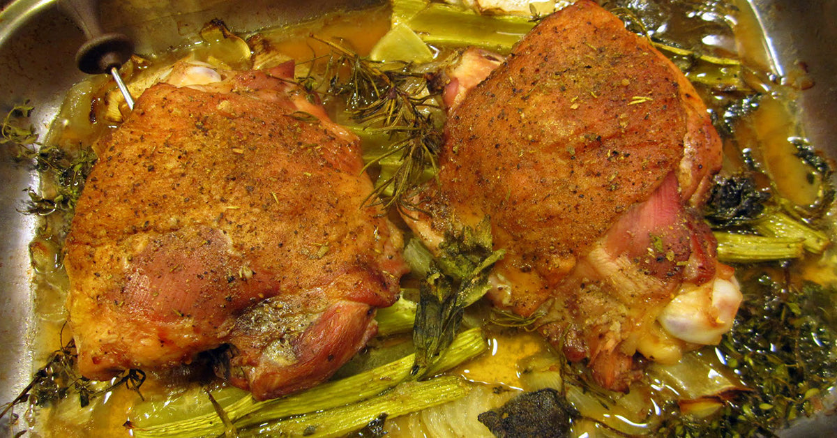 Roasted seasoned chicken thighs in a pan with herbs and vegetables.