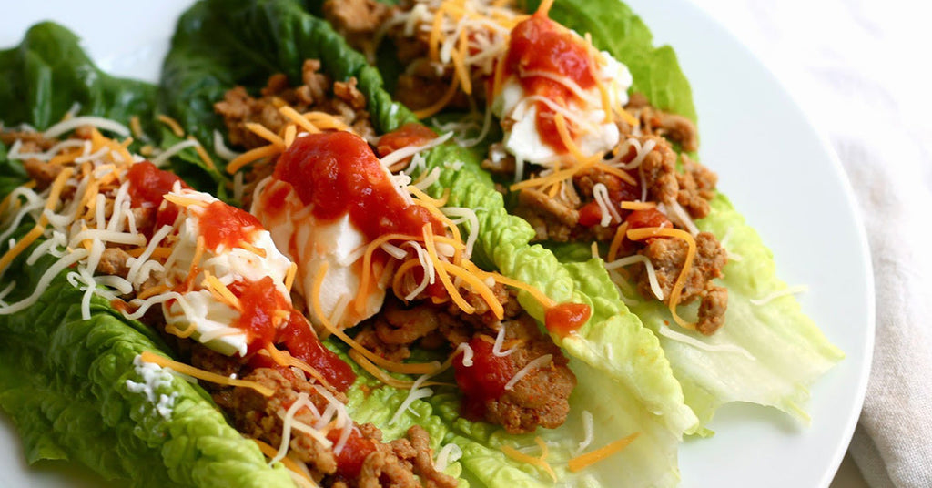 Lettuce wraps filled with seasoned ground meat, shredded cheese, salsa, and sour cream on a white plate.