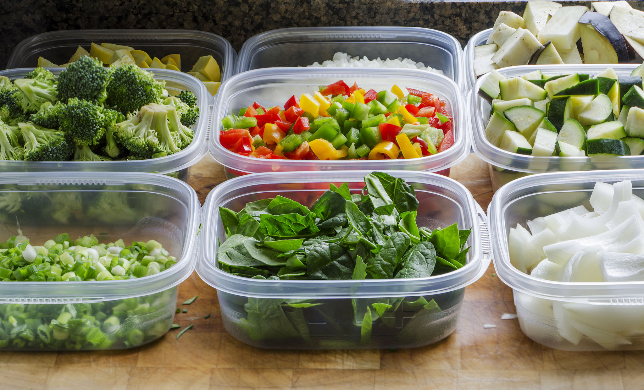 Assorted chopped vegetables arranged in clear containers, including broccoli, peppers, spinach, onions, and zucchini.