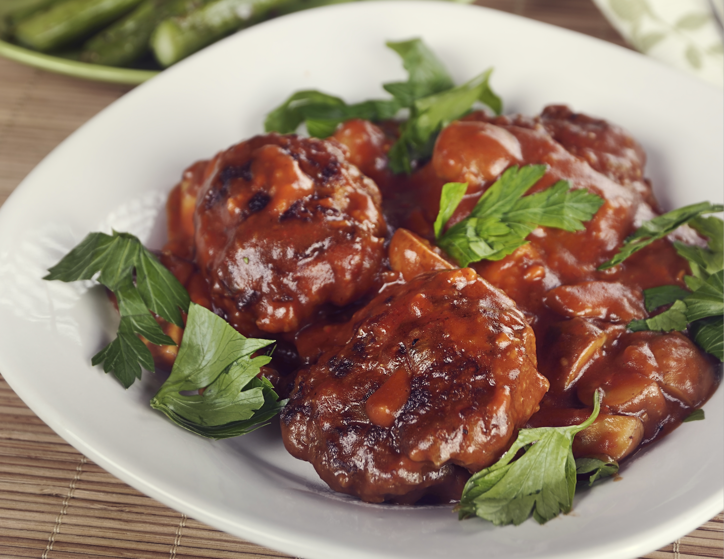 Plate of meat patties covered in rich brown sauce and garnished with fresh green herbs.