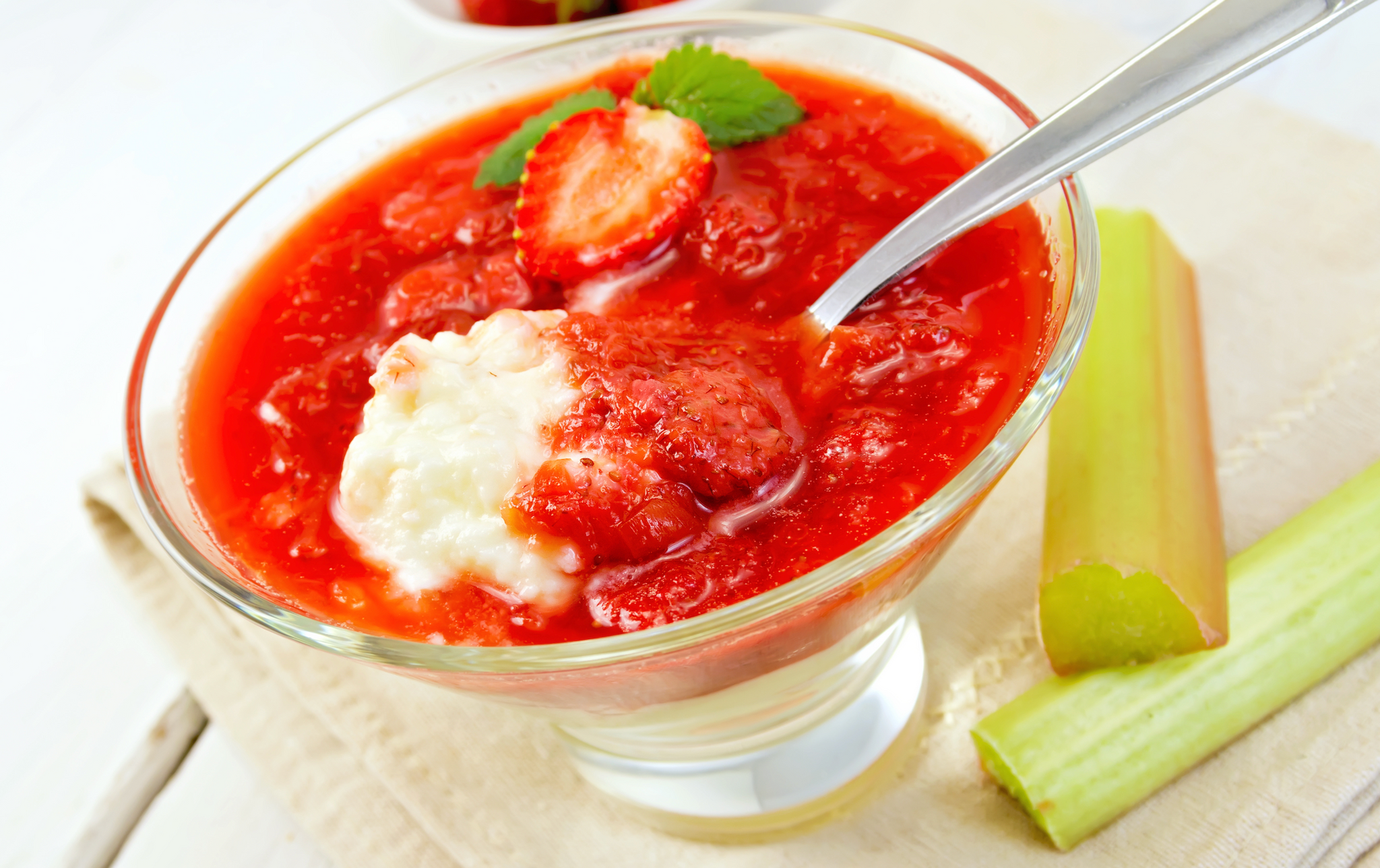 Bowl of strawberry–rhubarb dessert with creamy rice pudding and a spoon, garnished with a mint leaf.