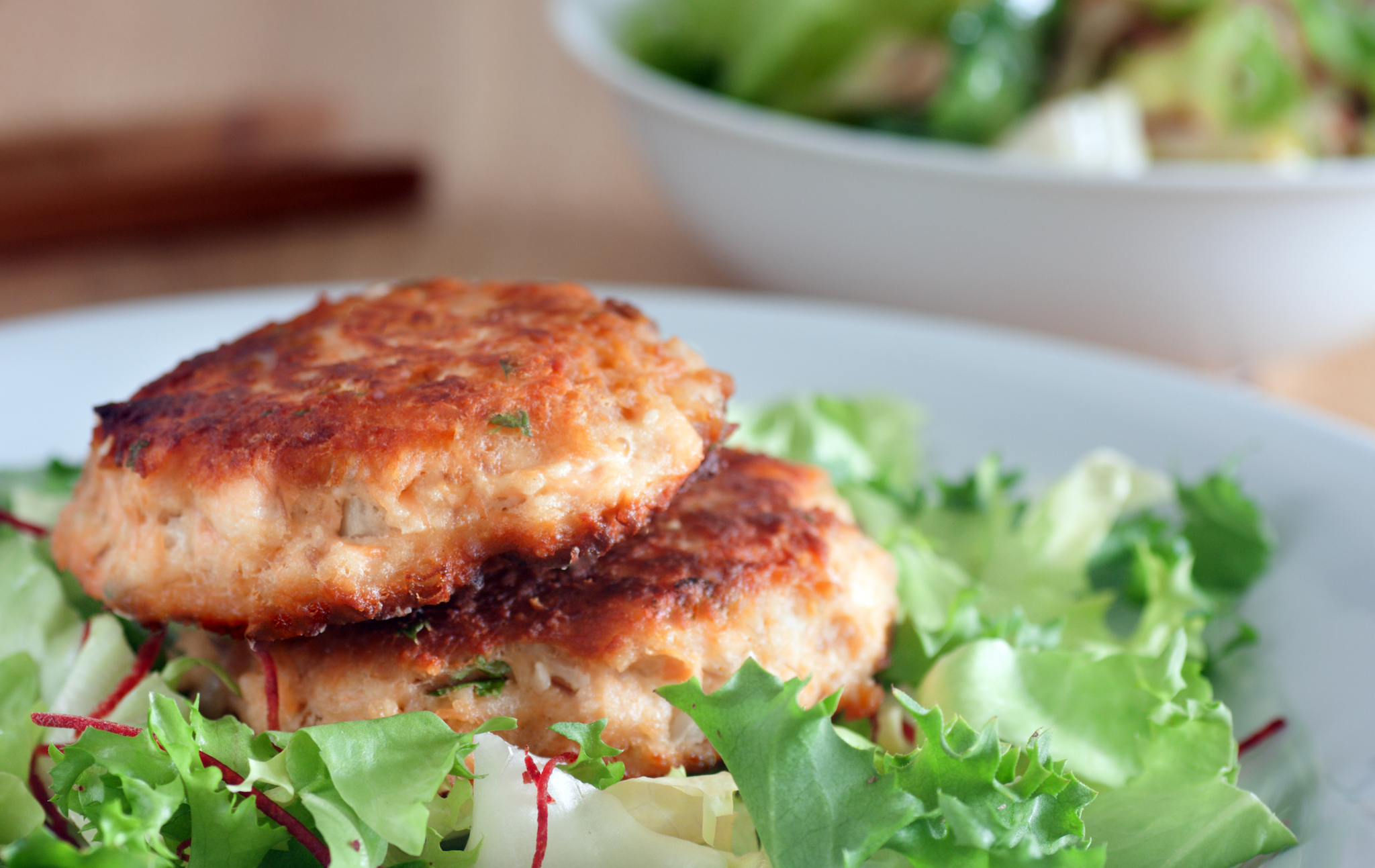 Two browned salmon patties served on a bed of fresh mixed greens.