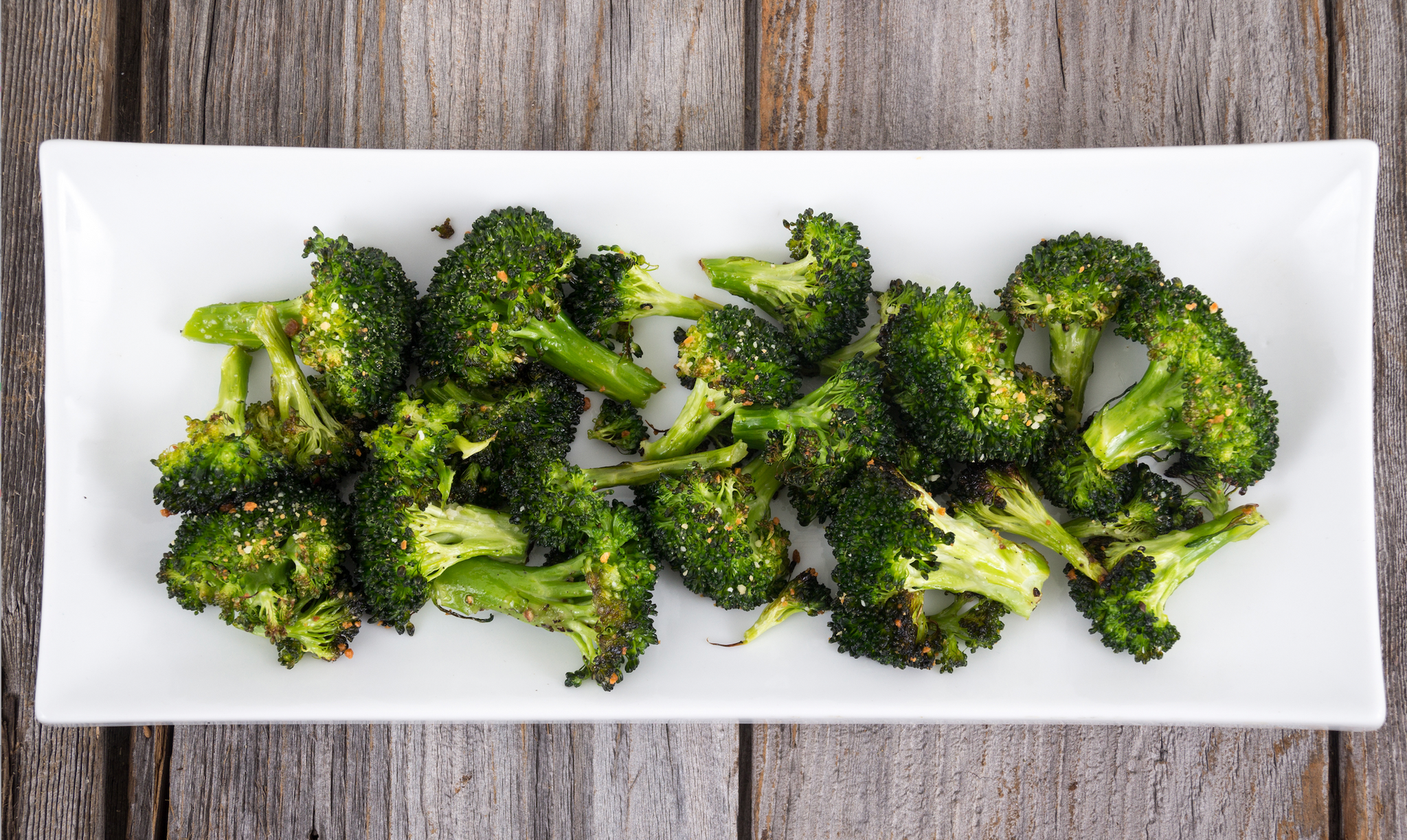 Roasted broccoli florets seasoned with herbs and spices on a white rectangular plate.