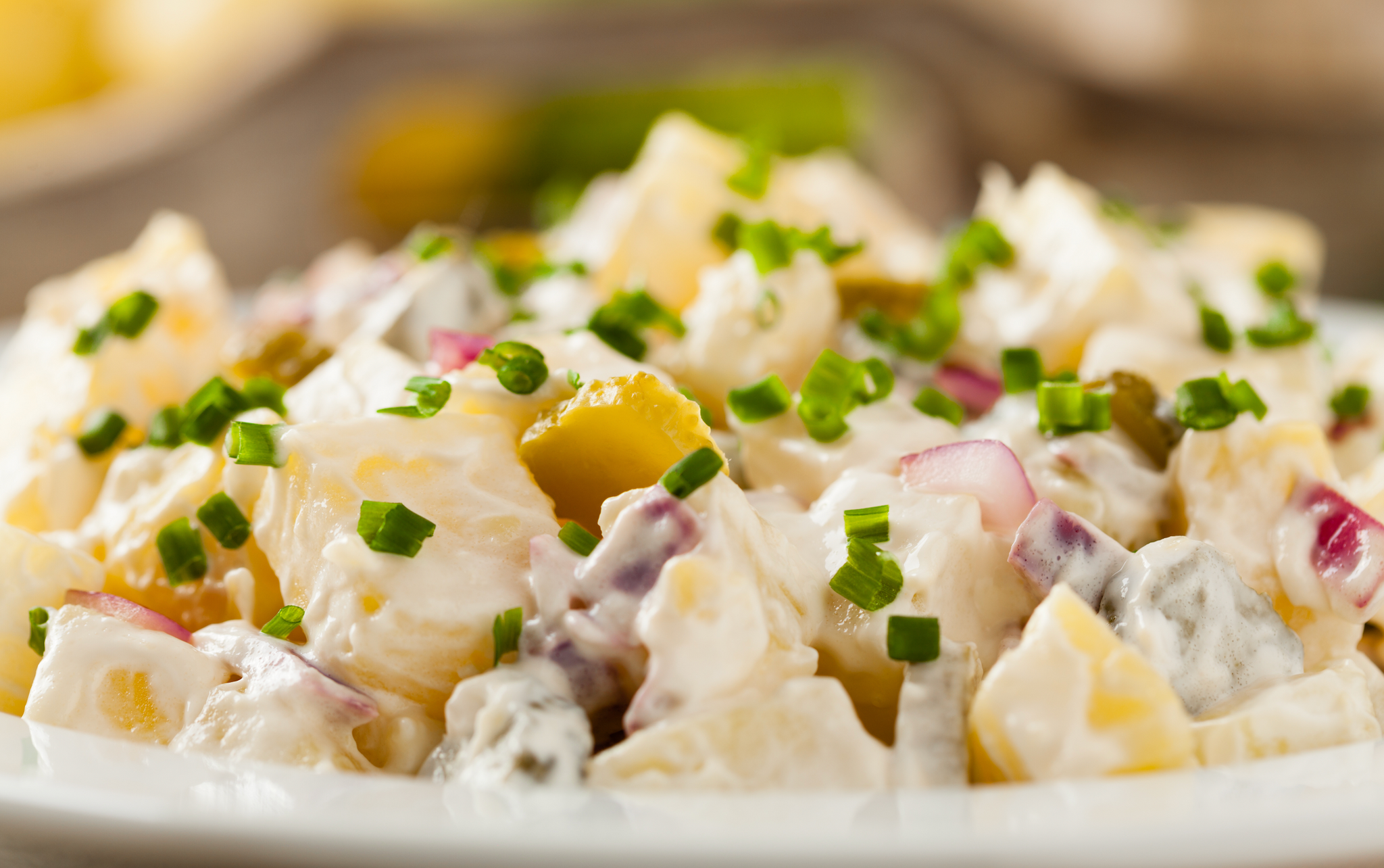 Close-up of creamy potato salad with chopped chives, red onions, and pickles.