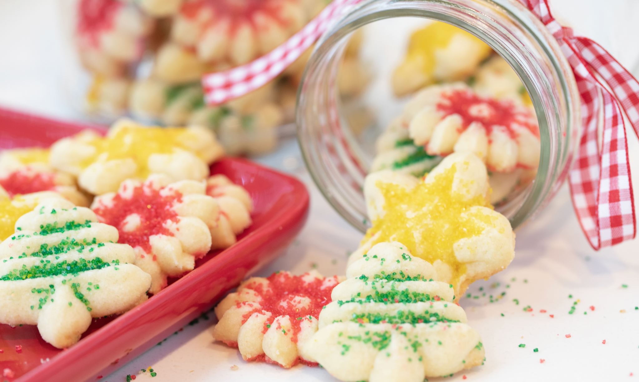 Colorful Christmas cookies with sprinkles spilling from a jar onto a tray.