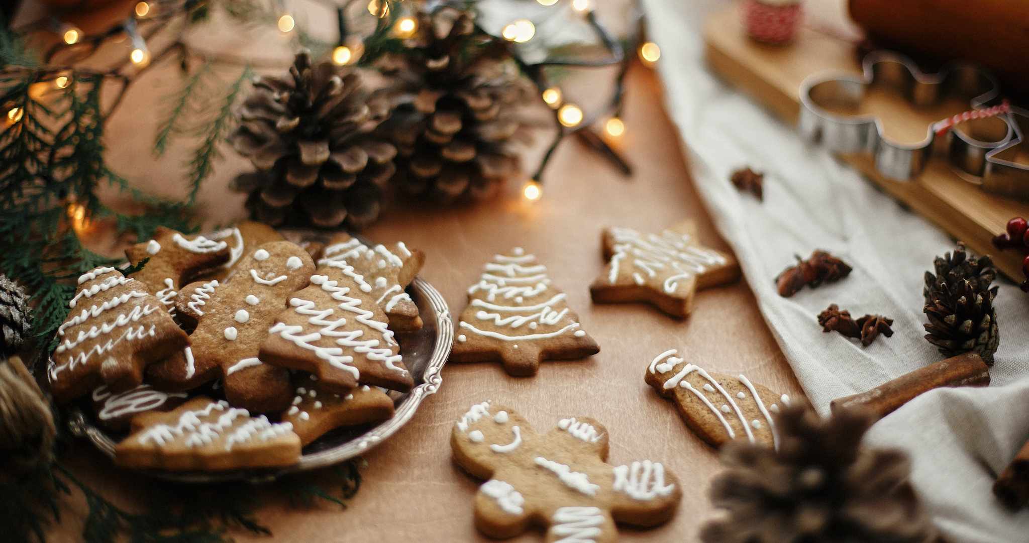 Iced gingerbread cookies shaped like trees and people on a festive table with pinecones and warm holiday lights.