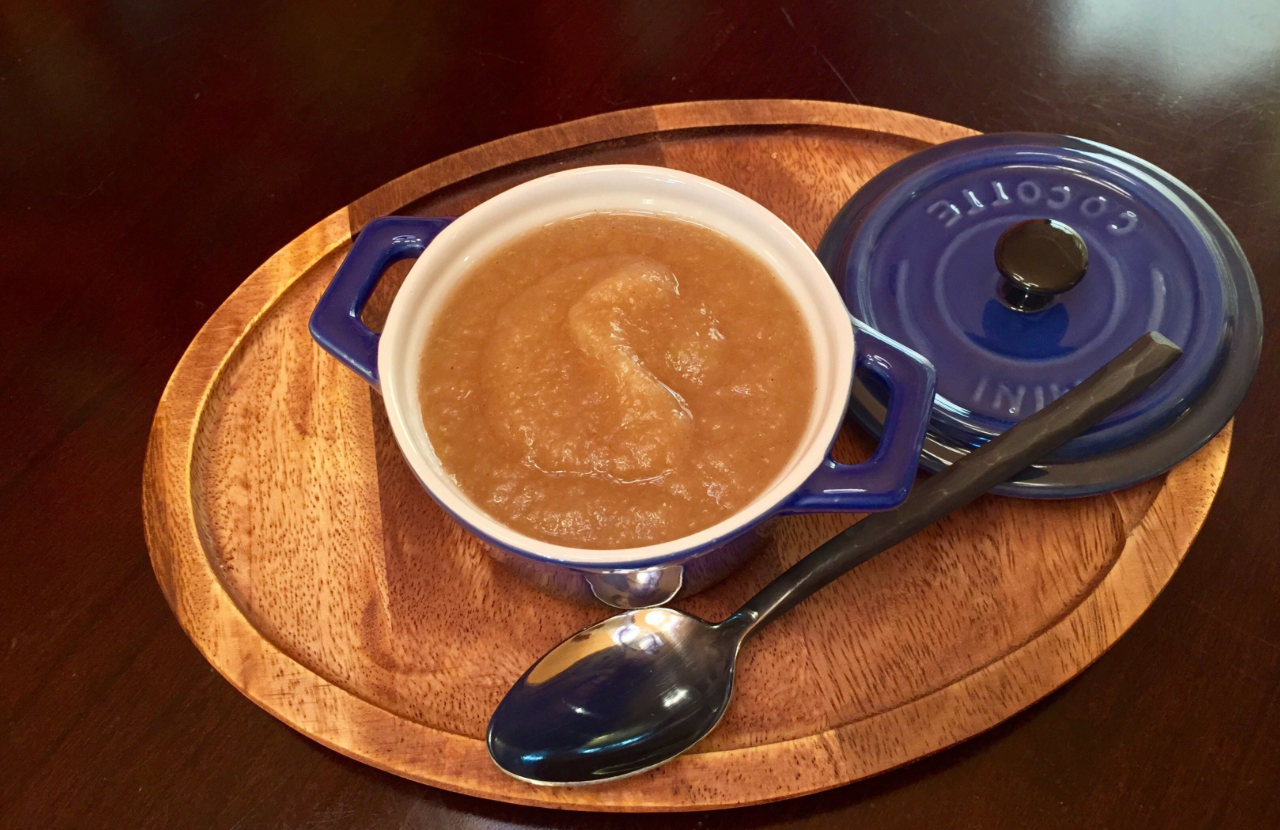 Bowl of applesauce in a blue dish on a wooden tray with a spoon and matching lid.