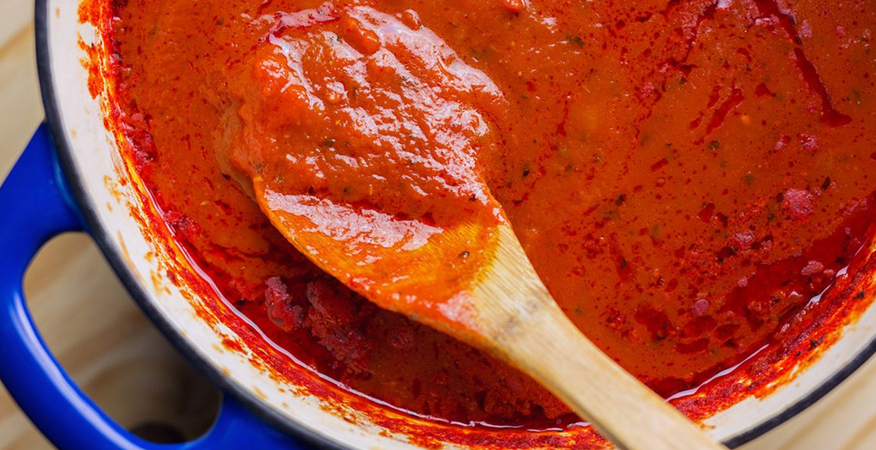 Thick red pasta sauce simmering in a pot with a wooden spoon coated in the rich, chunky mixture.