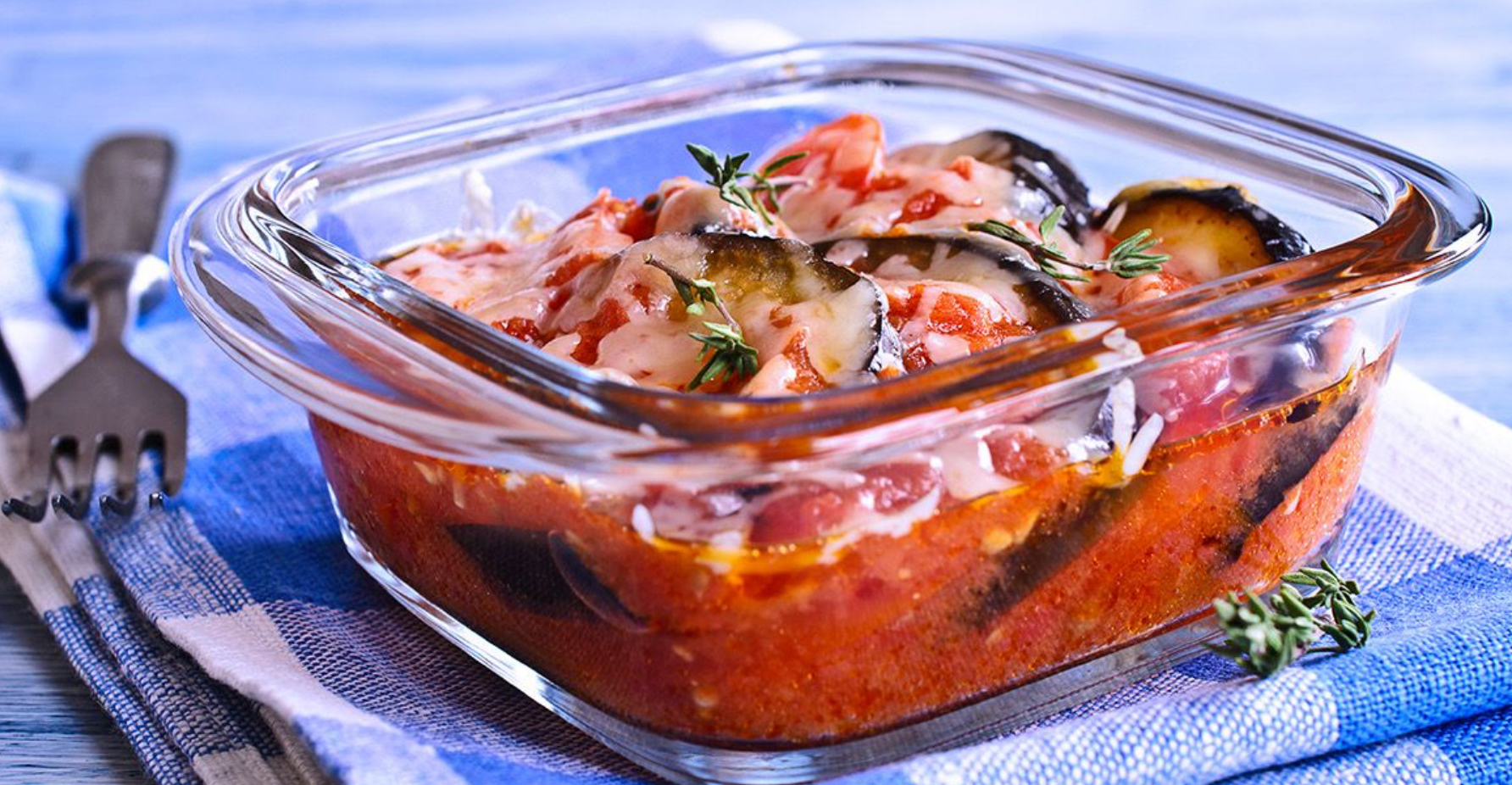 Glass baking dish filled with cheesy tomato and vegetable casserole topped with herbs.