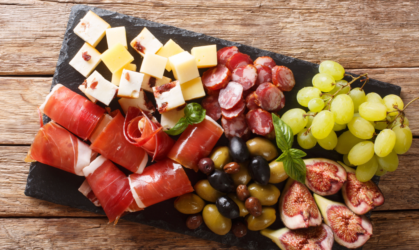 Charcuterie board with cured meats, cheeses, olives, grapes, and fresh figs on a dark slate.