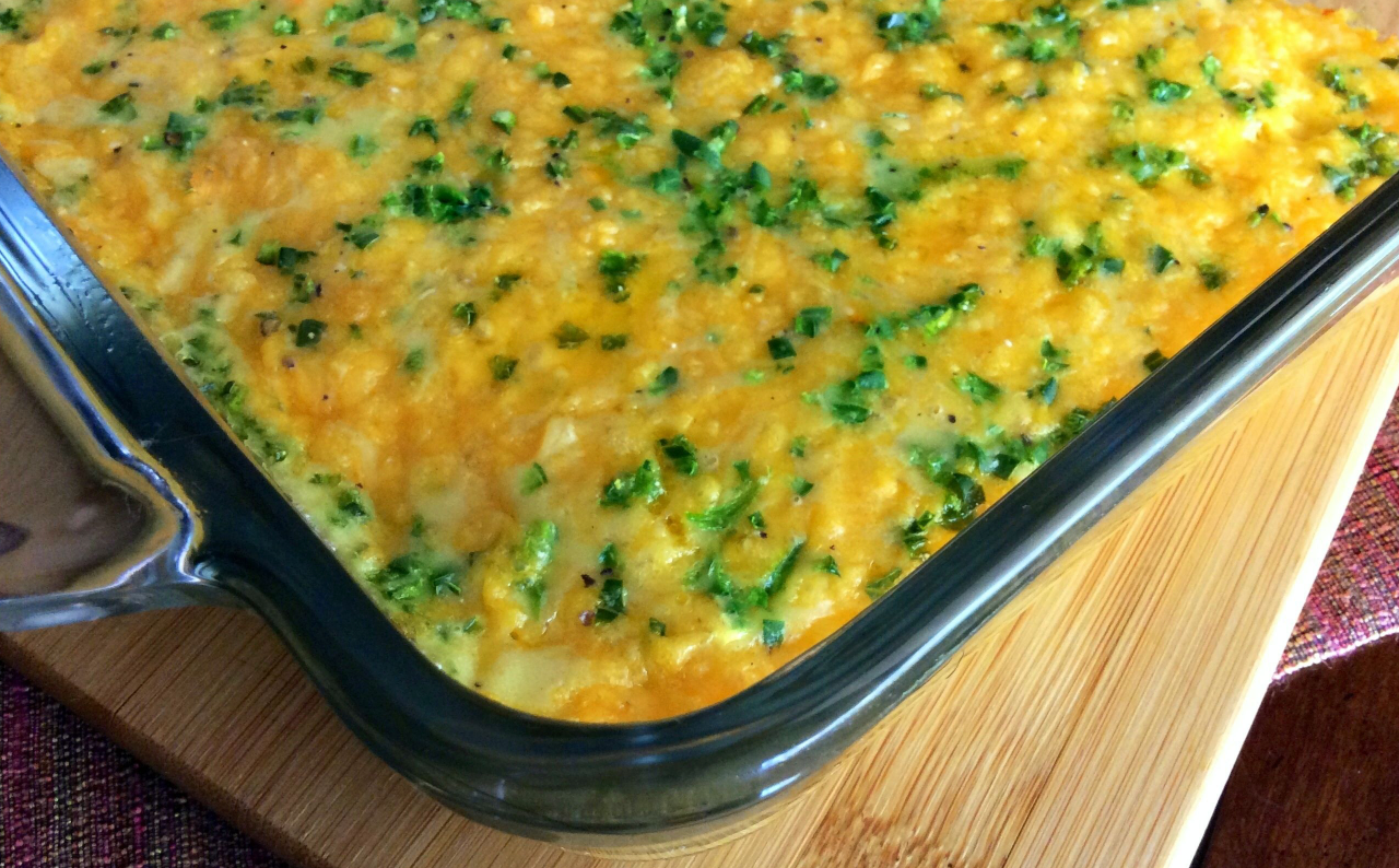 Baked casserole in a glass dish, topped with melted cheese and chopped green herbs on a wooden board.