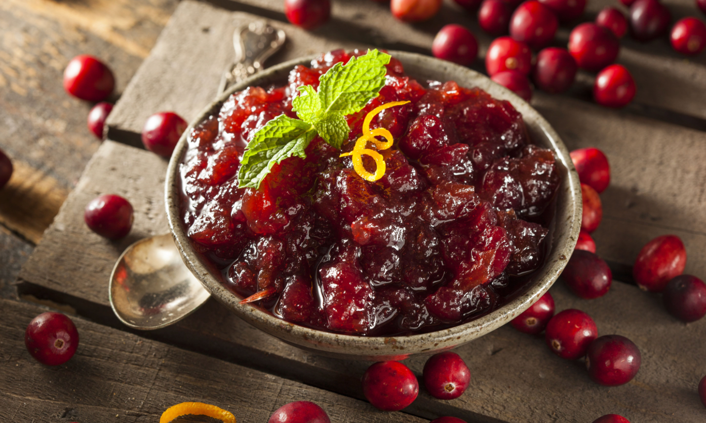 Bowl of chunky cranberry sauce topped with mint and orange zest, surrounded by fresh cranberries.