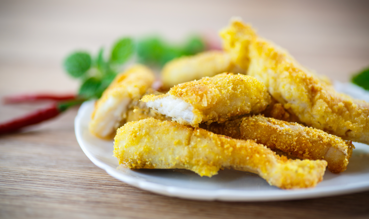 Crispy golden chicken strips piled on a white plate.