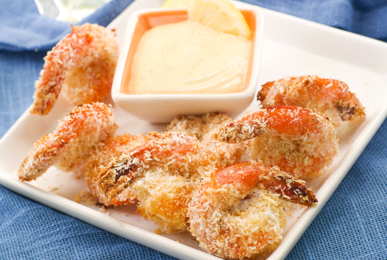 Crispy coconut-crusted shrimp arranged on a plate with a creamy dipping sauce and lemon slices.