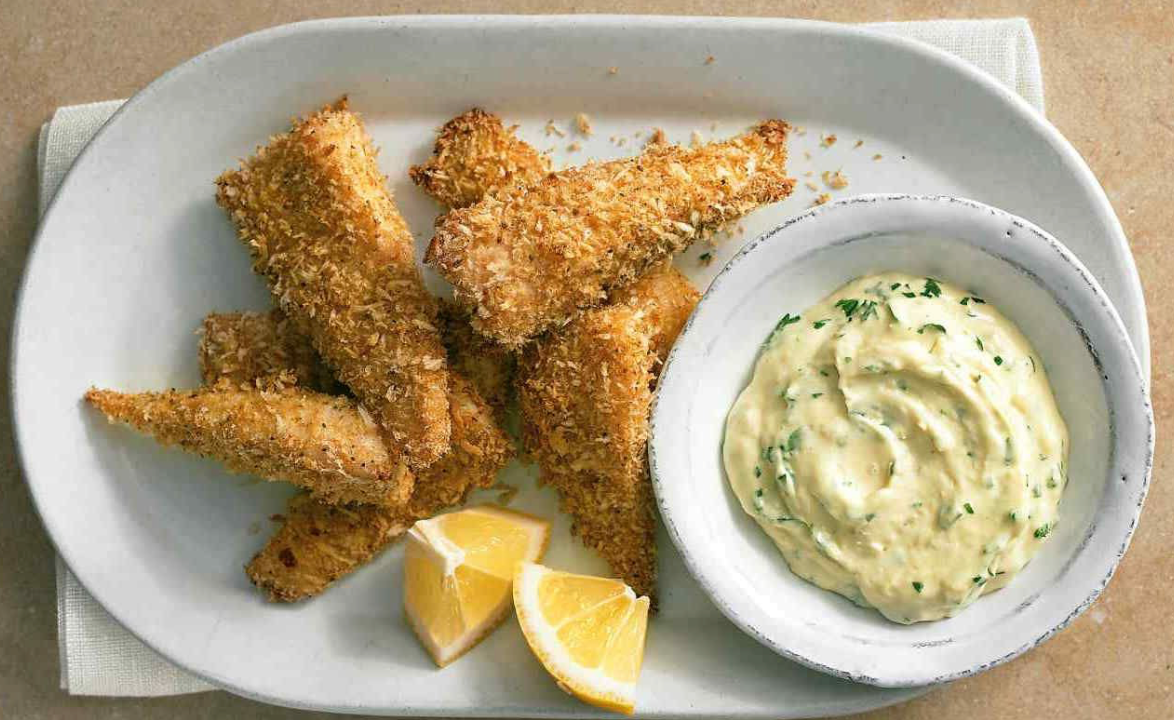 Crispy baked fish strips served with lemon wedges and a bowl of creamy herb dipping sauce.